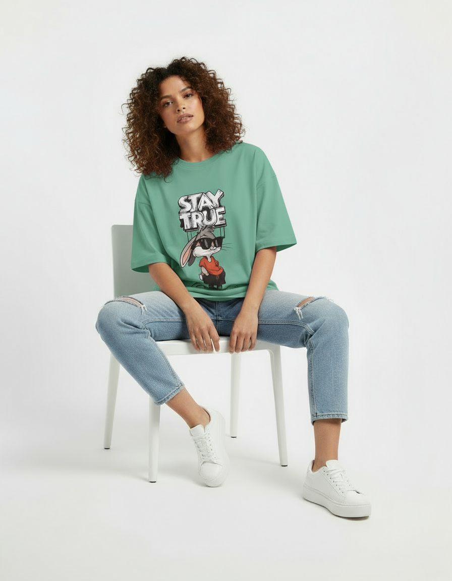 Person wearing a pink t-shirt with a graphic design, sitting on a white chair against a white background